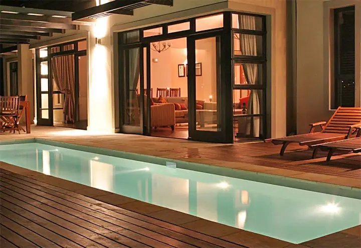 Covered outdoor timber deck beside a lit swimming pool