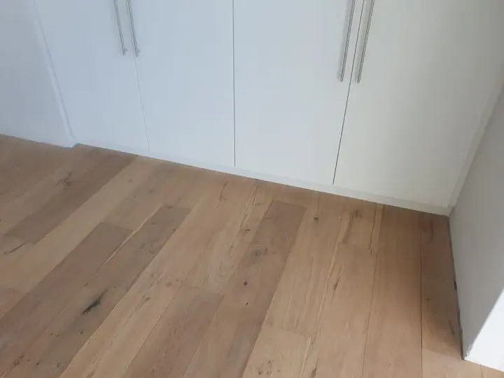 Light timber floorboards meeting white fitted cupboards