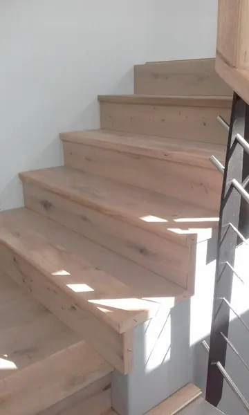 Pale timber staircase turning beside a steel railing